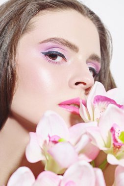 Orkide çiçekleri olan güzel romantik bir kadının yakın plan portresi. Makyaj ve makyaj malzemeleri. Güzellik ve sağlık hizmetleri.