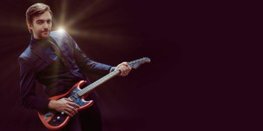 Klasik takım elbiseli duygusal neşeli genç müzisyen elektro gitarla rock 'n' roll çalıyor. Kopyalama alanı olan koyu arkaplan.