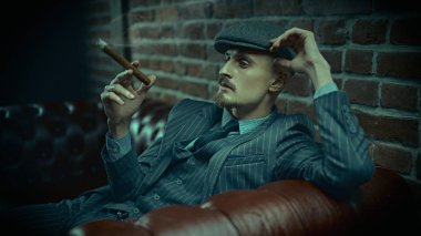 Yakışıklı, cesur bir adamın portresi zengin bir yerde, deri bir kanepede oturmuş puro içiyor. Lüks bir yaşam tarzı. Retro tarzı. Mafya ve suç dünyası, dedektif..