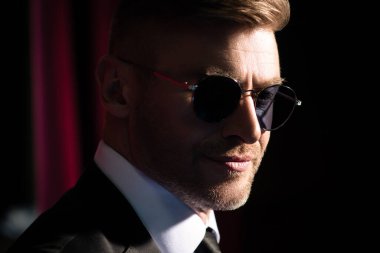 Güneş gözlüklü, gülümseyen, vahşi, yakışıklı bir adamın koyu renkli portresi. Erkek güzelliği, moda. Erkekler için optik.