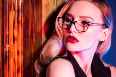Kırmızı ışıkta gözlük takan kendine güvenen bir kadının yakın portresi. Güzellik, makyaj, tarz.