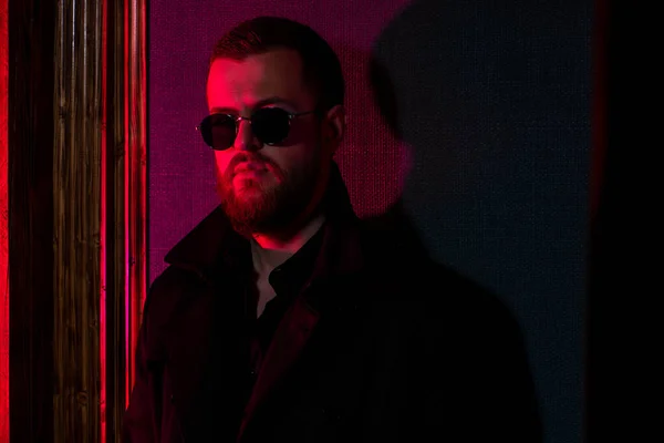 A dark portrait of a stylish man wearing sunglasses in red light. Beauty and style for men.