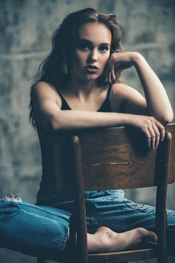 Stüdyoda sandalyede oturan güzel bir genç kadının portresi. Sıradan moda, güzellik..