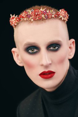 Kadın makyajlı solgun bir gencin portresi ve siyah bir arka planda kırmızı mücevherli taç.. 
