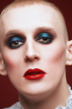 Kadın makyajlı solgun bir gencin portresi ve siyah bir arka planda kırmızı mücevherli taç.. 