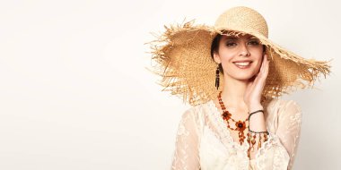 Zarif, dantelli bir elbise ve geniş kenarlı hasır bir şapkayla kameraya gülümseyen çekici bir genç kadının portresi. Moda fotoğrafı, yaz tarzı. Mutluluk.