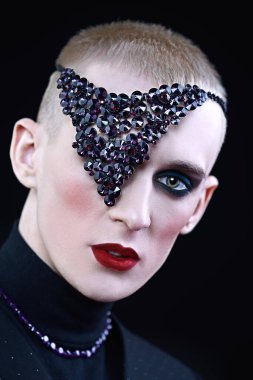 Kadın makyajlı, başında ve boynunda mor mücevher aksesuarları olan solgun bir gencin portresi..