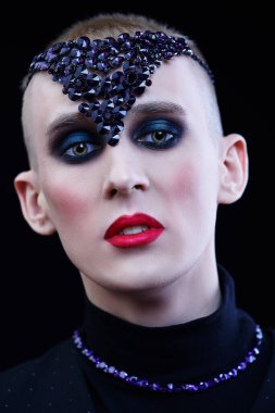 Kadın makyajlı, başında ve boynunda mor mücevher aksesuarları olan solgun bir gencin portresi..