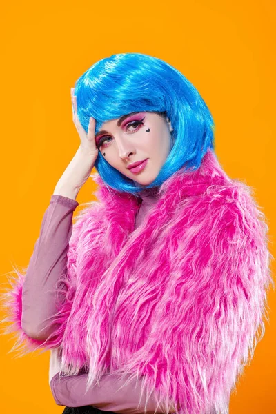 Portrait of an attractive party girl with bright pink makeup and blue wig wearing pink fur coat on a yellow background. Make-up and cosmetics, hairstyle. Fashion girl. Copy space.