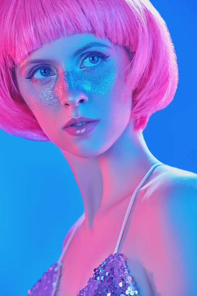 Beauty, makeup and cosmetics concept. Portrait of an attractive girl with shiny glitter freckles and a bright pink wig. Holiday and party style.