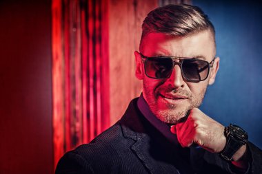 Güneş gözlüklü, gülümseyen, vahşi, yakışıklı bir adamın koyu renkli portresi. Erkek güzelliği, moda. Erkekler için optik.