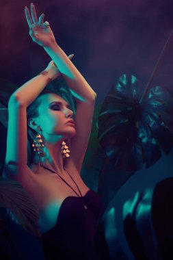 Islak saçlı güzel ateşli kadın tropikal bitkilerin arasında duruyor. Güzellik, moda ve kozmetik konsepti. Tropikal ülkelerde tatil.