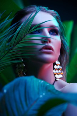 Palmiye yapraklarının arasında ıslak saçlı güzel bir tropikal kadının portresi. Güzellik, moda ve kozmetik konsepti. Tropikal ülkelerde tatil.