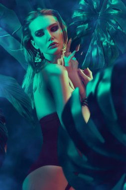 Islak saçlı güzel ateşli kadın tropikal bitkilerin arasında duruyor. Güzellik, moda ve kozmetik konsepti. Tropikal ülkelerde tatil.