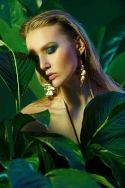 Palmiye yapraklarının arasında ıslak saçlı güzel bir tropikal kadının portresi. Güzellik, moda ve kozmetik konsepti. Tropikal ülkelerde tatil.