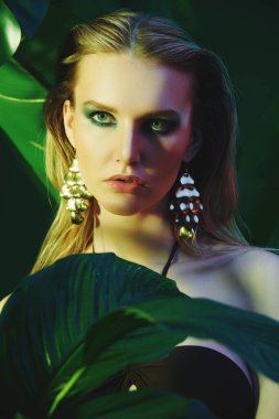 Palmiye yapraklarının arasında ıslak saçlı güzel bir tropikal kadının portresi. Güzellik, moda ve kozmetik konsepti. Tropikal ülkelerde tatil.