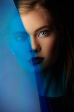 Stüdyoda siyah arka planda mavi bantla poz veren güzel, zarif genç bir kadın..