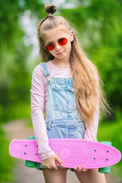 A portrait of an active teenager girl posing on the road with a skateboard. Casual kids fashion, active lifestyle, beauty.