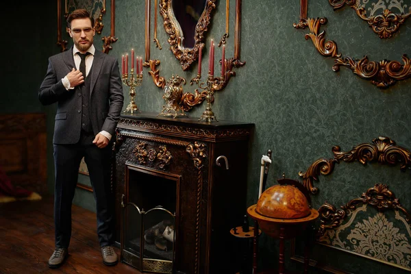 Handsome gentleman poses in a tweed suit and glasses in a vintage interior. Luxurious lifestyle. Vintage style. Full length.