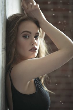 Genç ve güzel bir kadının portresi stüdyoda duvarın arkasında poz veriyor. Sıradan moda, güzellik, optik.