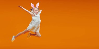 Sarı arka planda sevinçten zıplayan parlak yaz kıyafetleri içinde mutlu beş yaşındaki bir kız. Mutlu bir çocukluk. Boşluğu kopyala. 