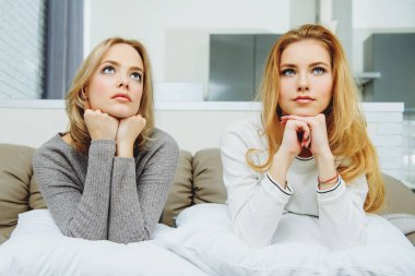 İki kız arkadaş evdeki kanepede yastıkla evde oturuyorlar..