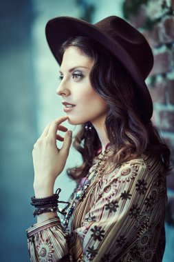 Boho tarzı elbise ve aksesuar giymiş mutlu bir kızın portresi harabe duvarların arka planına poz veriyor, yosunla kaplanmış. Bohem, modern hippi tarzı..