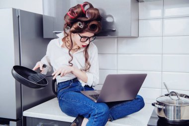 Saçında bigudilerle günlük kıyafetlerle güzel bir kız defterdeki tarife bakıyor ve eş zamanlı olarak hazırlanıyor. Moda ev çekimi. Pin-up tarzı.