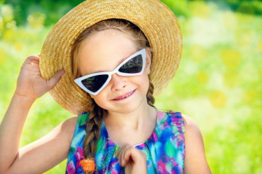 Hasır şapkalı ve güneş gözlüklü güzel kız bir yaz parkında duruyor. Güneşli bir gün.