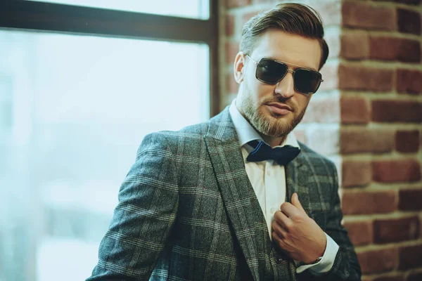 Handsome man in elegant checkered suit and sunglasses in a modern loft interior. Luxurious lifestyle. Man's fashion.