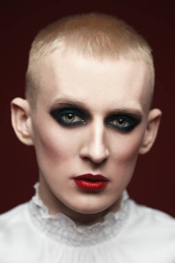  Kırmızı arka planda poz veren kadın makyajlı genç bir adamın portresi..