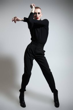 Kadın makyajlı ve kadın kıyafetleriyle stüdyoda ifade ile poz veren genç bir adamın tam boy portresi.. 