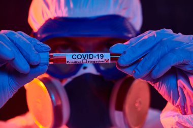 COVID-19 veya 2019-NCoV. Korumalı PPE kıyafeti giymiş bir mikrobiyologun yakın plan portresi, koronavirüse karşı aşıyı gösteriyor. Aşılama.