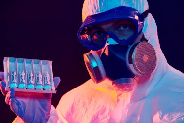 COVID-19 veya 2019-NCoV. Koruyucu PPE kıyafetli bir mikrobiyolog olan doktor koronavirüse karşı aşısı olan ampuller gösterdi. Aşılama.