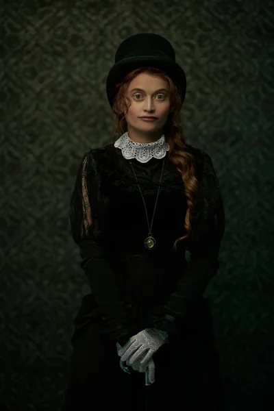 Beautiful Victorian woman in black dress and top hat stands in vintage interior. Steampunk.