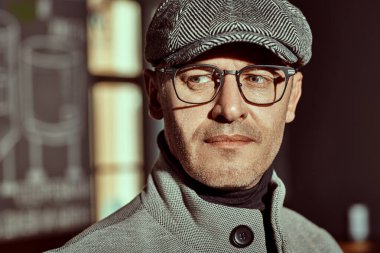 Pencerenin yanında duran zarif kıyafetler ve gözlüklerle yakışıklı orta yaşlı bir adamın yakın plan portresi. Erkek güzelliği, moda. Optik biçimi.