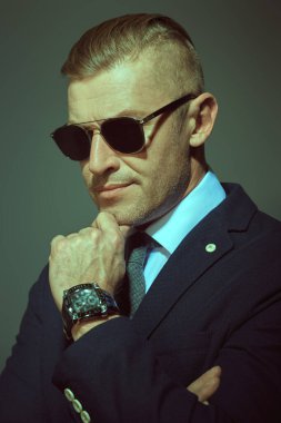 Gri arka planda güneş gözlüğü ve takım elbiseli saygıdeğer olgun bir adamın portresi. İş adamı portresi.