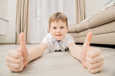 COVID-19 ve yaşam konsepti. Sevimli çocuk evde yerde yatan parmaklarını gösteriyor. Koronavirüs sırasında karantina.