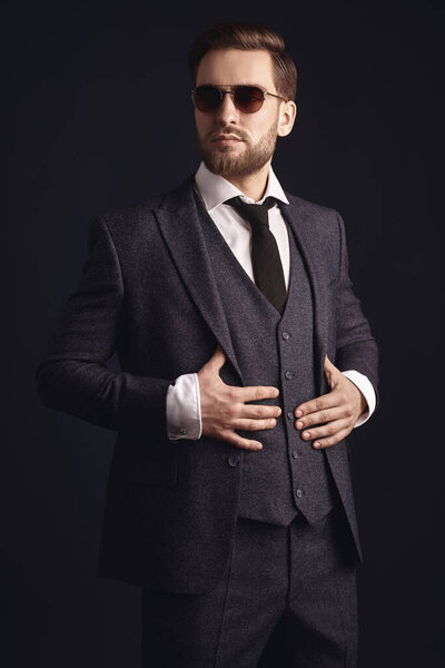 Portrait of a handsome businessman wearing elegant suit and sunglasses on a black background. Men's beauty, fashion. Optics for men. 