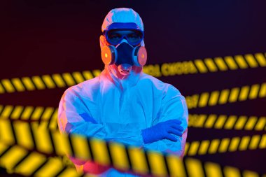 COVID-19 kavramı. Koruyucu kıyafetli bir tıp çalışanı kısıtlayıcı bantların arkasında duruyor. Tecrit ve karantina.