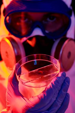 COVID-19 veya 2019-NCoV. Koruyucu PPE kıyafetli bir bilim adamının yakından çekilmiş portresi kan testini bir petri kabında gösteriyor..