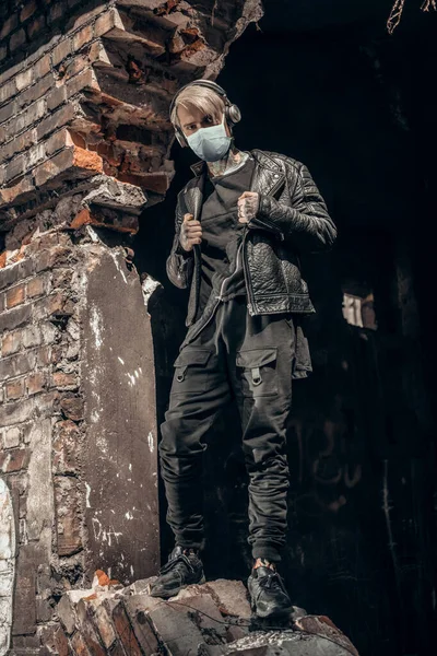 COVID-19 pandemic virus infection worldwide. A young man in a mask stands on the background of a destroyed building.