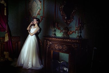 Zarif, beyaz, uzun elbiseli, cep telefonuyla konuşan muhteşem genç bir kadının tam boy portresi. Lüks karanlık daireler. Düğün modası.