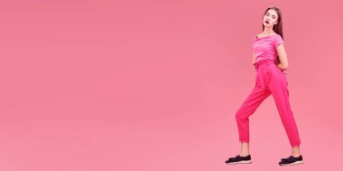 Stüdyoda son moda kırmızı tişört ve pembe arka planda pantolonla poz veren güzel bir manken. Göz kamaştırıcı pembe bir tarz. Tam boy portre. 