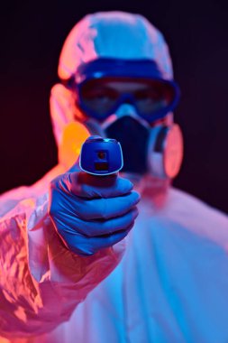 Coronavirus veya COVID-19 konsepti. Koruyucu PPE kıyafetli bir doktorun portresi elinde termometreyi kırmızı ve mavi bir arkaplanda tutuyor.. 