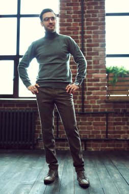 Gündelik giysiler içinde yakışıklı genç bir adam pencerenin yanında durur ve mutlu bir şekilde gülümser. Erkek güzelliği, moda. İş adamı portresi. Erkekler için optik.