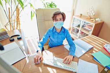 Coronavirus ve yaşam. Tıp maskeli erkek öğrenci COVID-19 yüzünden karantina nedeniyle evde kalıp öğreniyor..