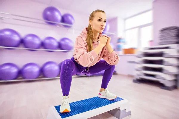 Sports and health concept. Beautiful athletic girl is working out in the gym. Step aerobics, fitness.