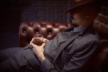 Yakışıklı sarhoş bir adam deri koltukta bir bardak viskiyle rahatça oturuyor. Lüks bir yaşam tarzı. Retro tarzı. Mafya ve suç dünyası. 