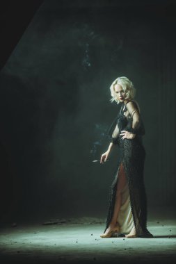 Sigara içen sarışın güzel bir kadının uzun bir portresi. Gece elbisesi. Moda, güzellik.